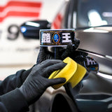 Person applying Soft99 The King of Gloss wax to a black car using a yellow applicator sponge.