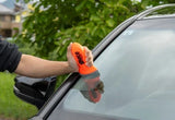 A person using an orange Glaco glass cleaning tool on a car windshield.