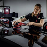 Woman using FLEX polisher on glossy black car in detailing garage