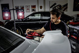 Man using FLEX polisher on white car in garage with detailing tools and lights