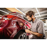 Man using cordless orbital polisher on red car for premium car detailing in garage