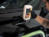Detailer applying Meguiar's car polish to glossy black vehicle hood with gloved hand