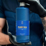 A person in black gloves holding a bottle of Labocosmetica PURIFICA Acid Decontaminant Shampoo.
