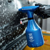 A person in black gloves using a blue Labocosmetica spray bottle on a soapy car.