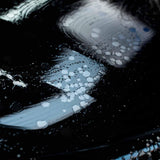 Close-up of Labocosmetica PURÌFICA shampoo foam and bubbles on a black car surface.