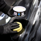 Applying Soft99 The King of Gloss wax to a black car using a sponge applicator.