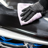 A gloved hand using a purple microfiber cloth to polish a black car with Soft99 gloss wax.