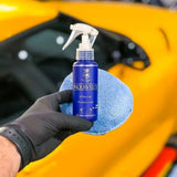 Hand in black glove holding Labocosmetica AQUAVÈLOX Glass Nano Sealant with a blue microfiber cloth.