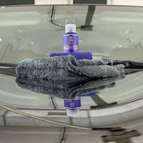 Labocosmetica AQUAVÈLOX Glass Nano Sealant bottle with a grey microfiber towel on a car windshield.