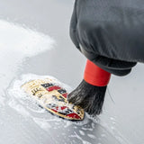 Using a detailing brush with Labocosmetica ÈNERGO to remove stains from a car emblem.