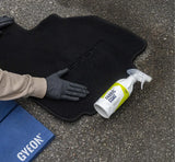 Applying Gyeon Fabric Coat ceramic protector to black Porsche car mat with gloved hand