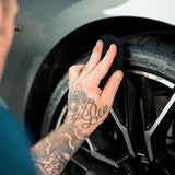 A person using a microfiber cloth to apply Labocosmetica HYDRA dressing to a car tire.