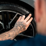 Close-up of a person applying Labocosmetica HYDRA sealant to a car tire with a microfiber cloth.