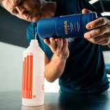 A person pouring Labocosmetica PRÌMUS 2.0 alkaline prewash into a dilution bottle.