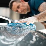 Person using a blue microfiber wash mitt with foam to clean a car surface with Labocosmetica.