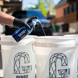 Person in black gloves pouring Gyeon Q²M Bathe+ car shampoo into a white wash bucket.