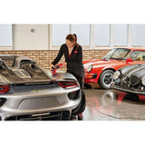Woman polishing silver sports car in garage alongside classic red and black cars, car detailing